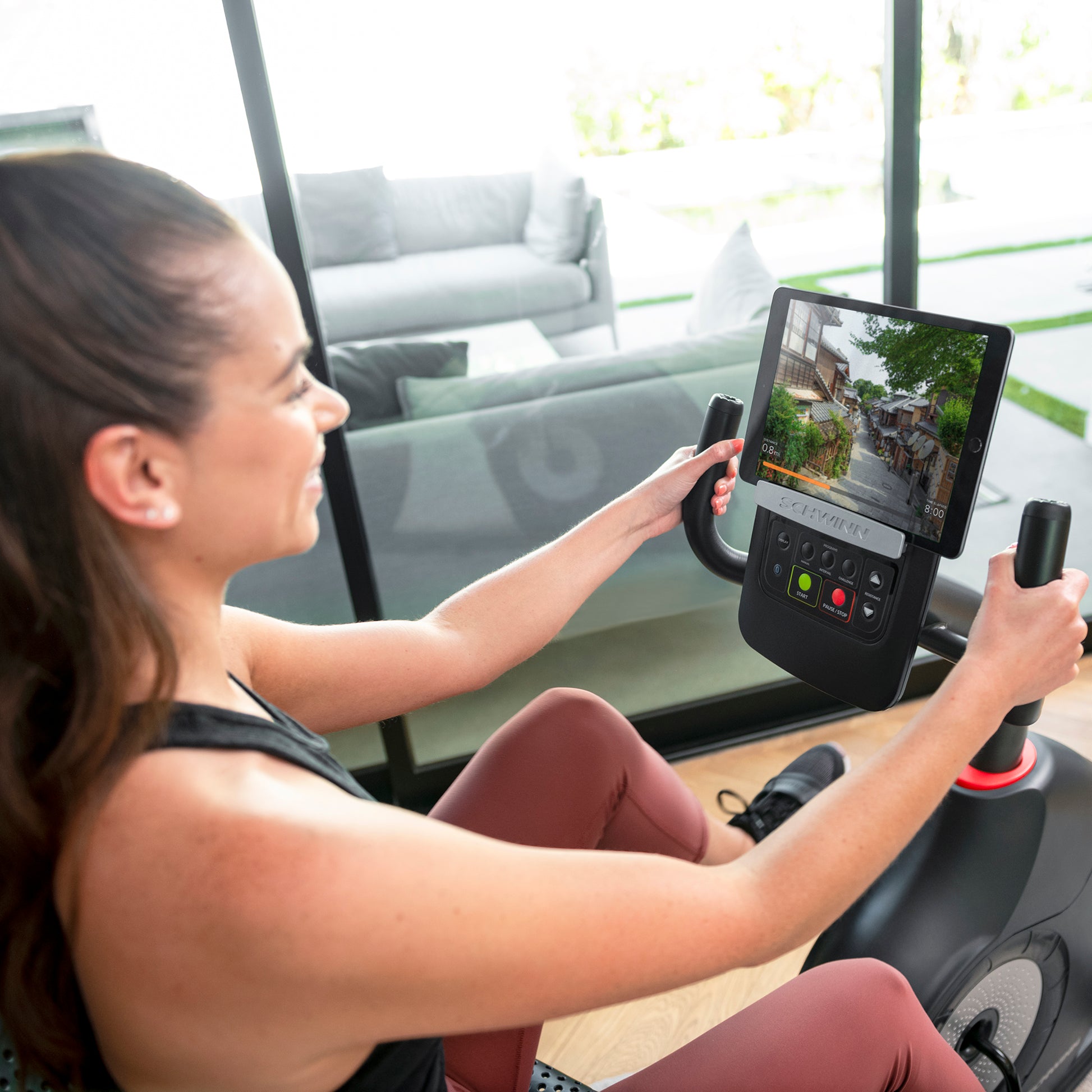 Woman using a stationary bike with a tablet displaying a video game.