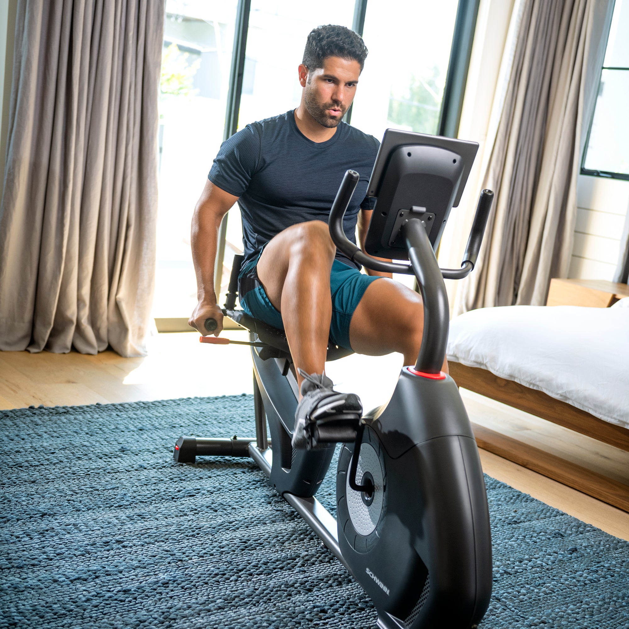 Man exercising on a stationary bike in a bedroom.