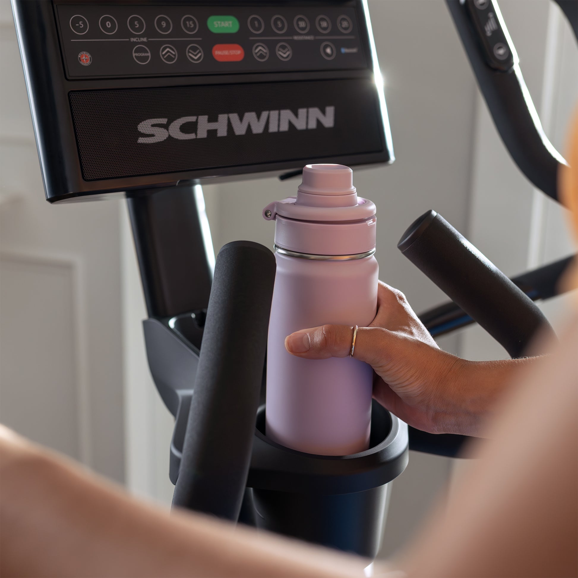 Person placing a pink water bottle in a Schwinn elliptical cup holder.