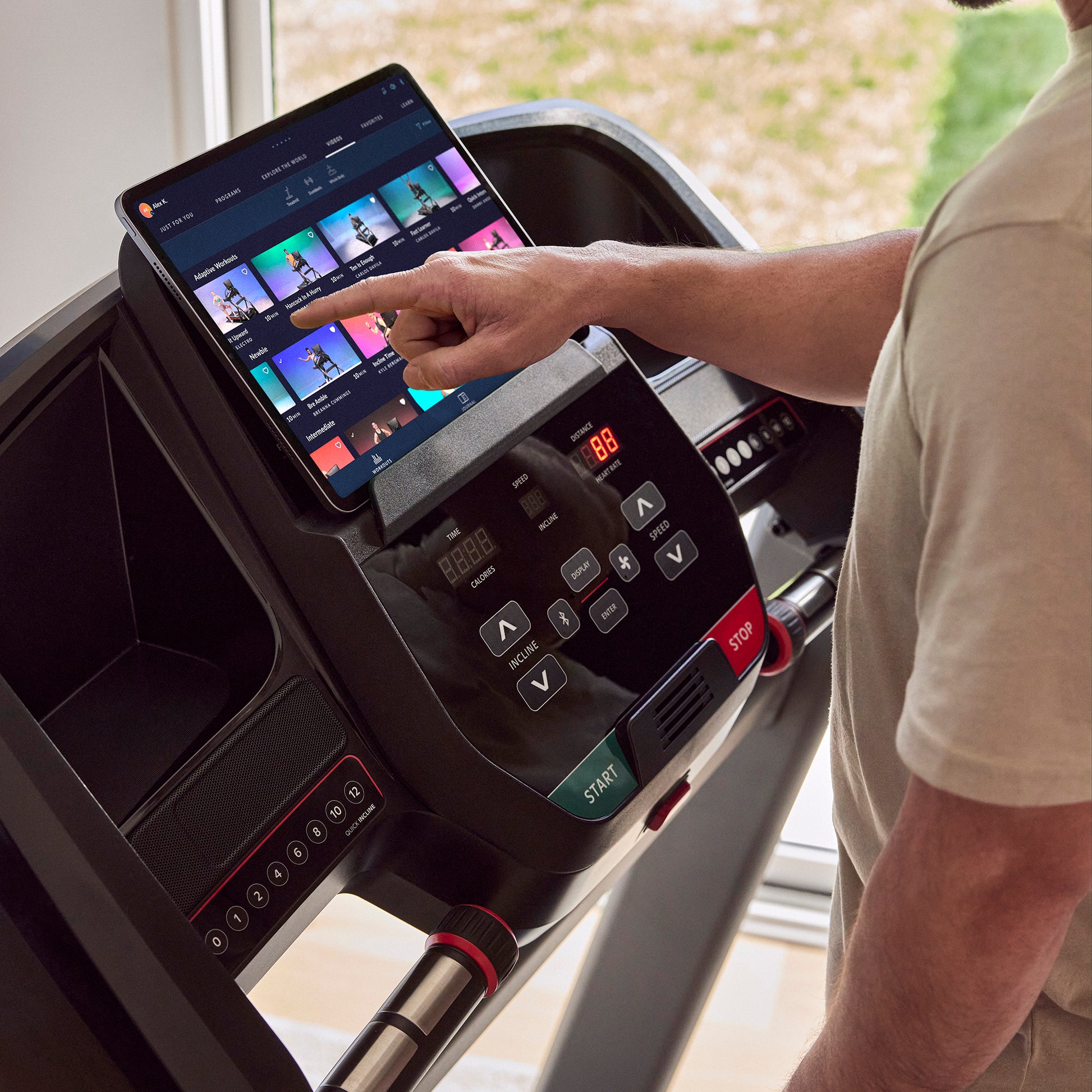 Person using a treadmill with a tablet displaying a fitness app.